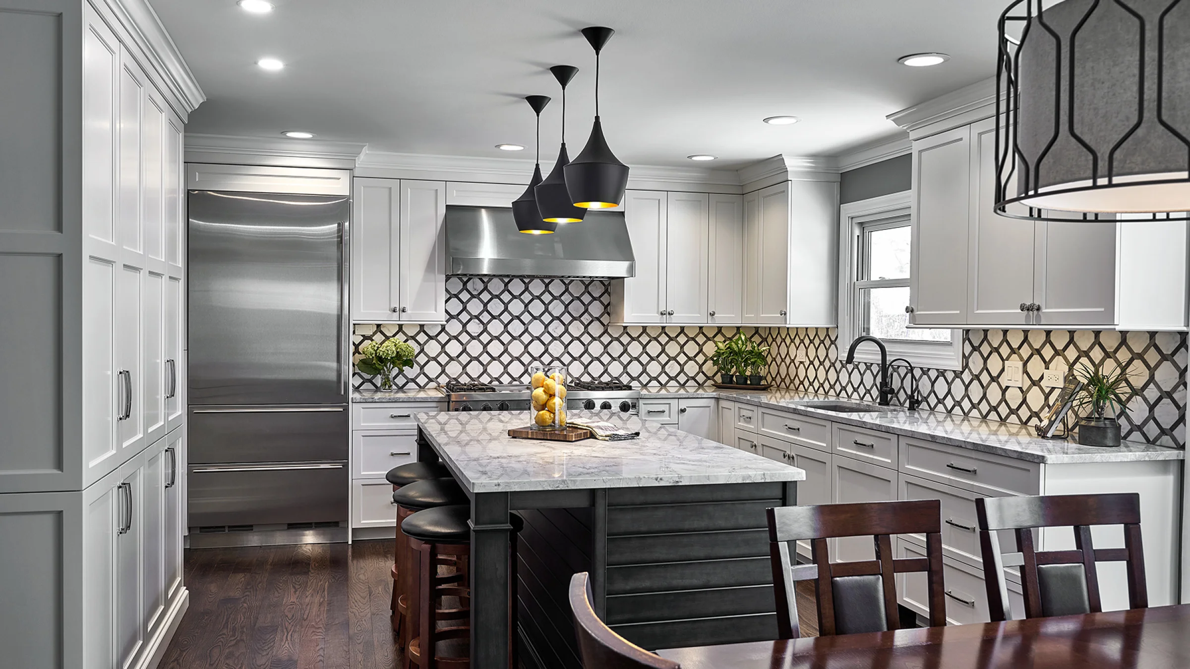 Modern kitchen remodel featuring white cabinets, marble countertops, dark island, wood floors, and pendant lighting.