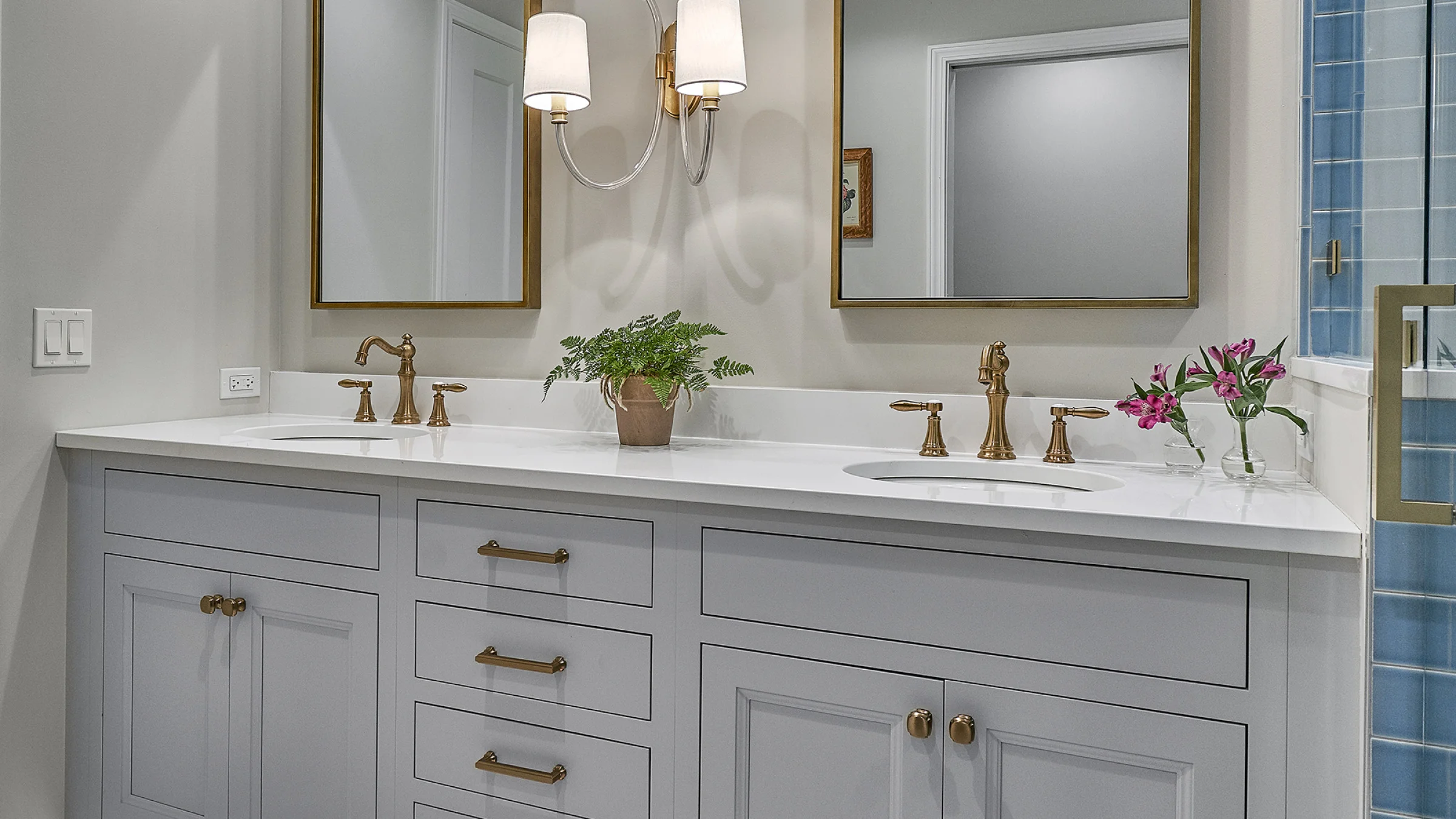 Western Springs bathroom remodel: gray vanity, white quartz countertop, gold faucets, mirrors, and blue tile shower.