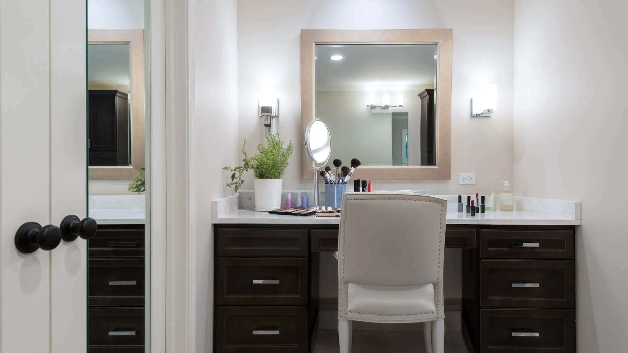 Modern bathroom vanity with dark wood cabinets, white countertop, makeup, mirror, and chair in Palatine, IL.