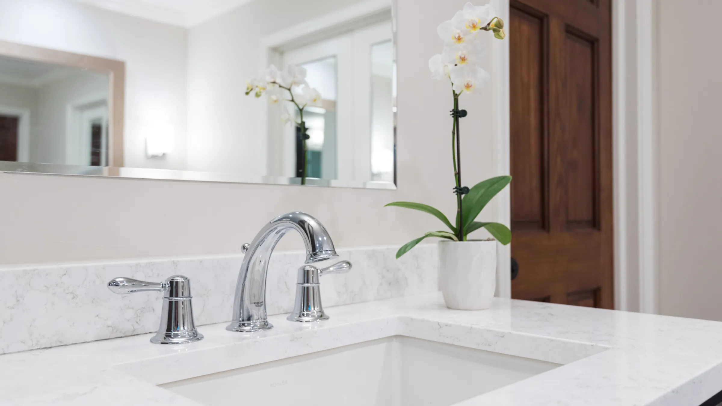 Modern primary bathroom vanity with marble countertop, chrome faucet, and elegant orchid plant.