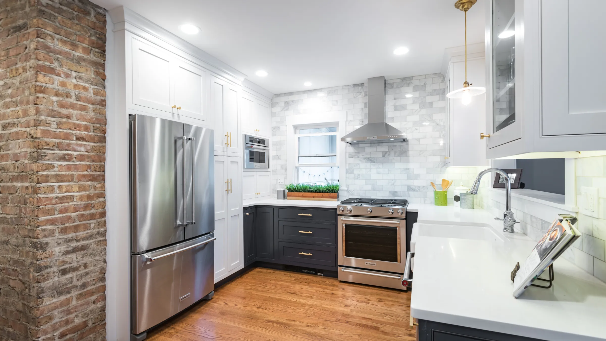 Remodeled kitchen with white cabinets, dark lower cabinets, stainless steel appliances, marble backsplash, and wood floors.