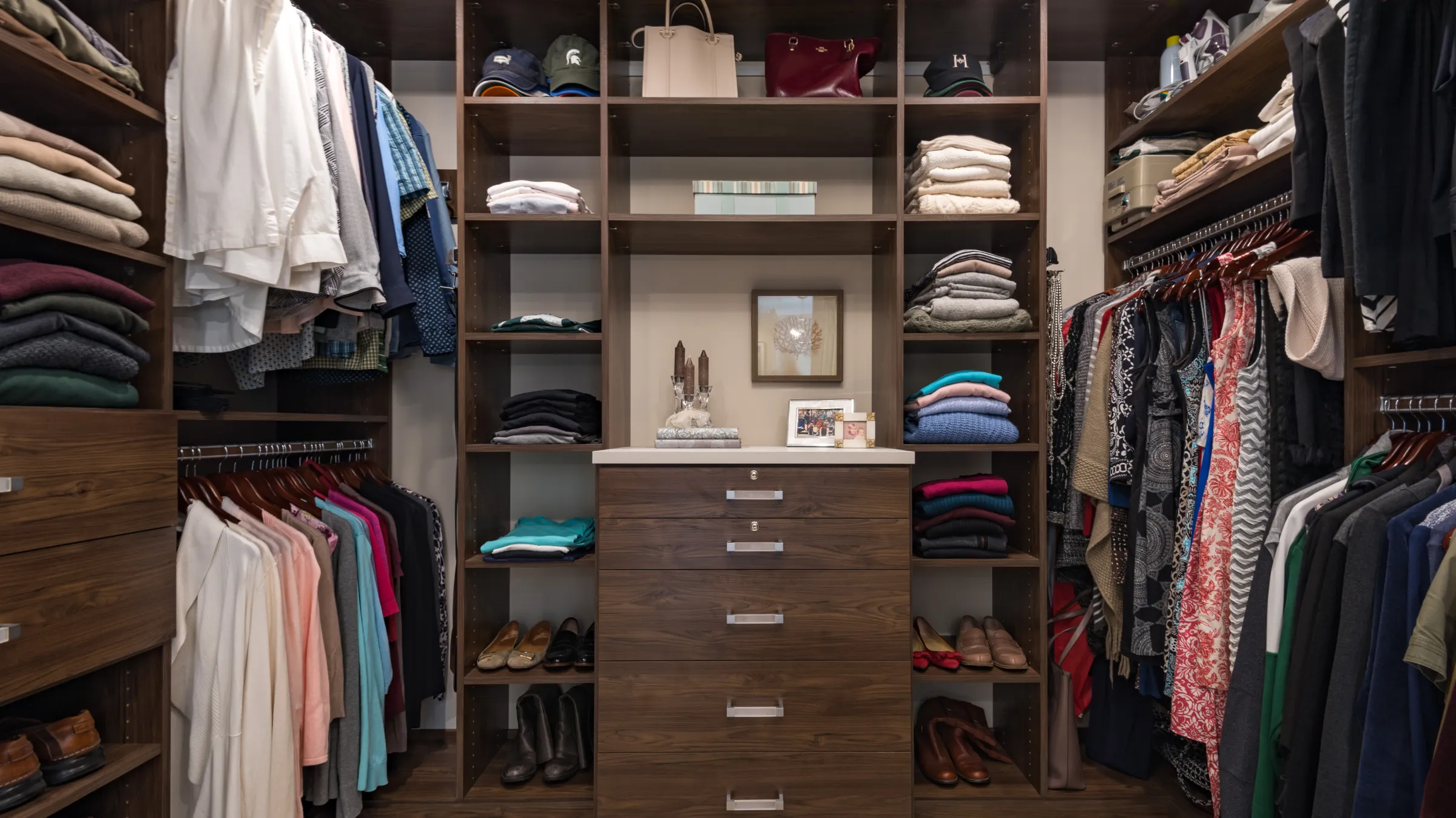 Custom closet with organized shelving, drawers, and hanging clothes. Dark wood cabinetry.