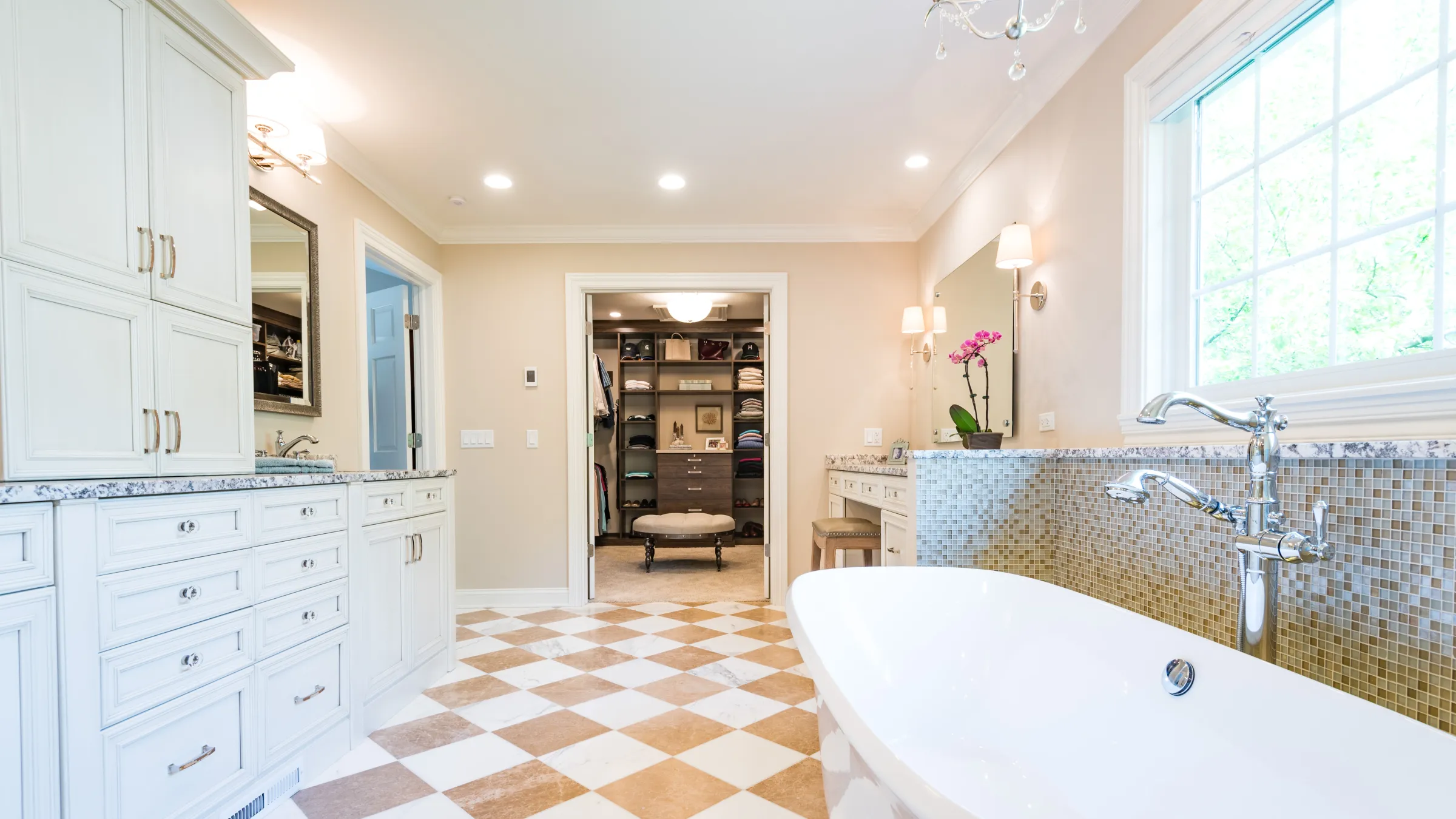 Luxurious primary bath remodel featuring custom white cabinets, mosaic tile, freestanding tub, and checkered tile flooring.