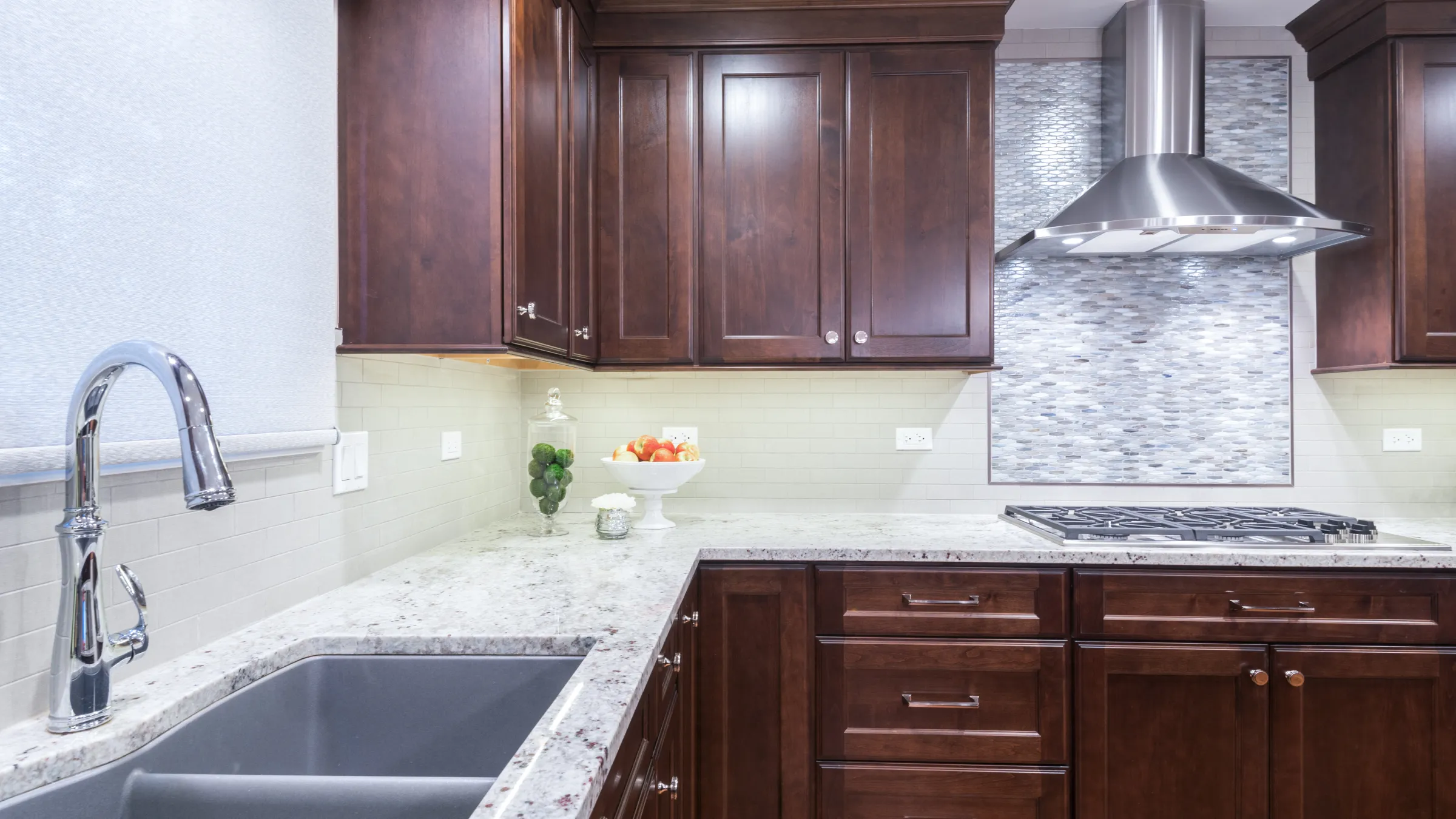 New kitchen features dark wood cabinets, granite countertops, a stainless steel range hood, and a stylish sink faucet.