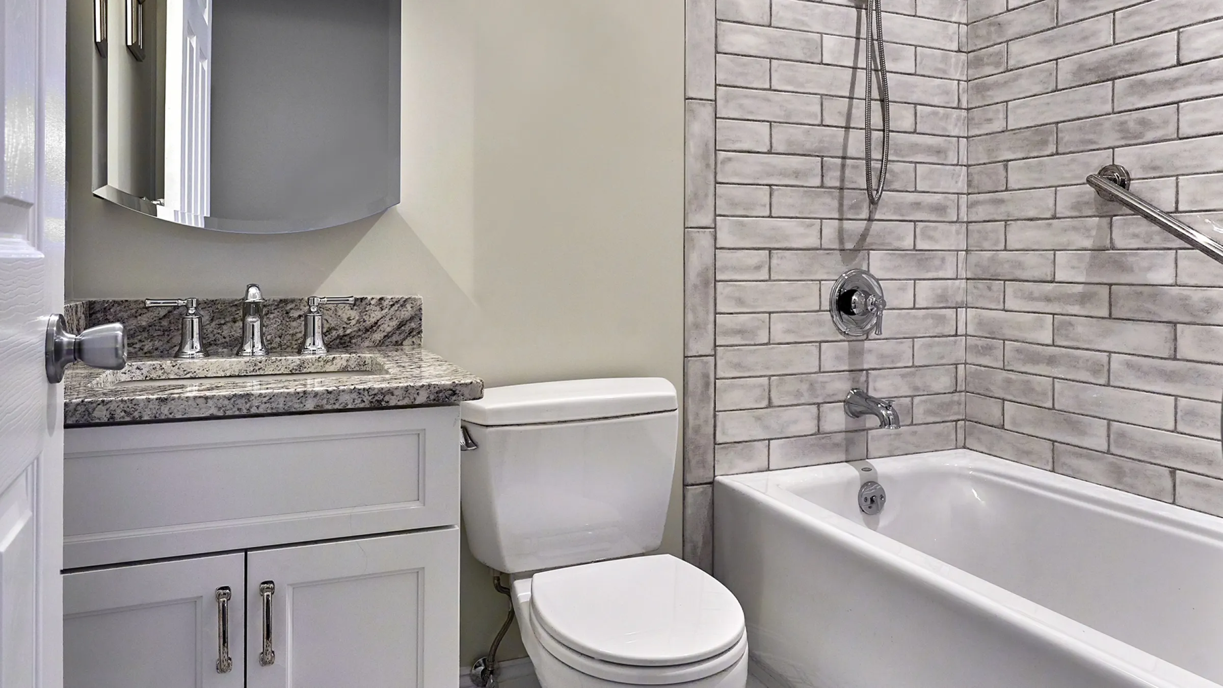 Remodeled bathroom with granite countertop, white cabinets, subway tile shower, and white toilet.