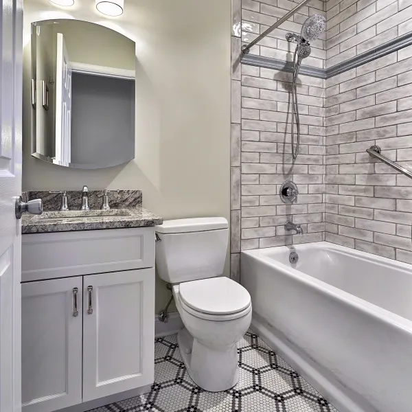 Remodeled bathroom with granite countertop, white cabinets, subway tile shower, and white toilet.