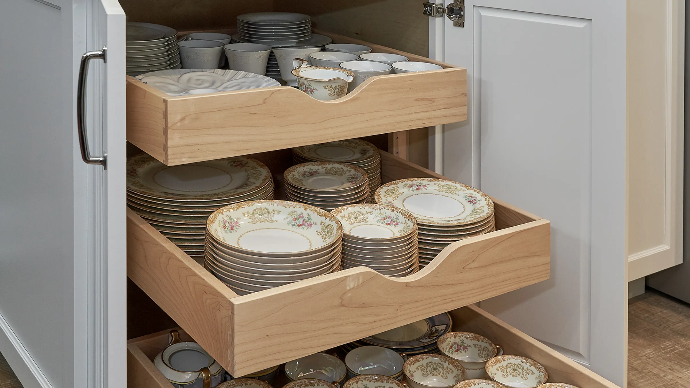 Kitchen cabinet with pull-out drawers holding dishware. Remodeled kitchen storage solution.