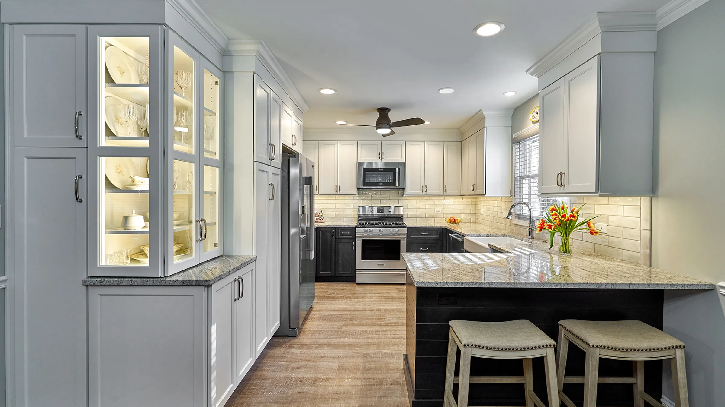 Remodeled kitchen with white cabinets, granite countertops, wood floors, and a breakfast bar with two stools.