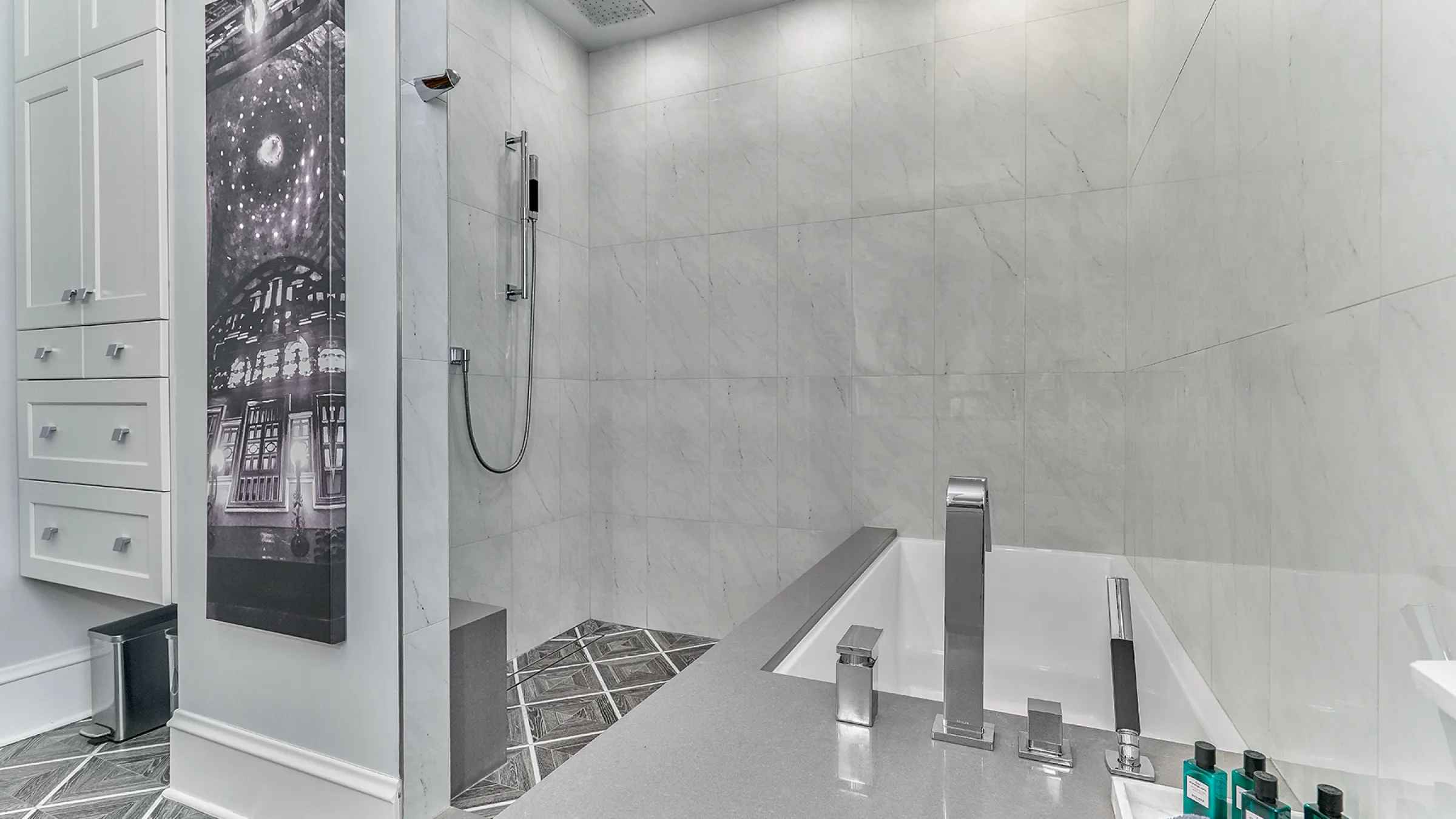 Modern bathroom renovation with walk-in shower, soaking tub, gray countertops, custom cabinets, and patterned tile floor.