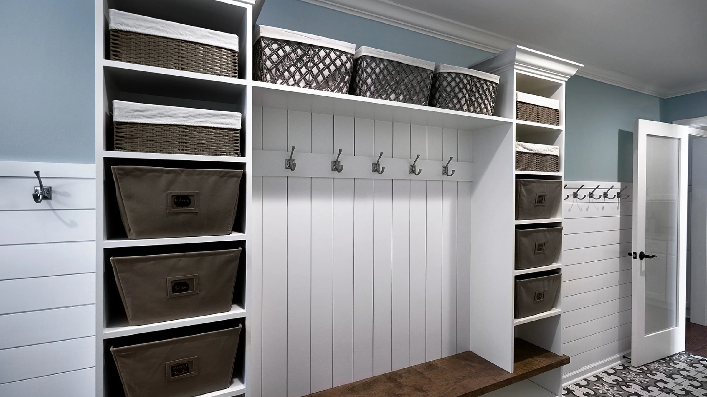 Custom mudroom built-in with storage baskets, bench, hooks, and white shiplap. Inverness, IL home renovation.