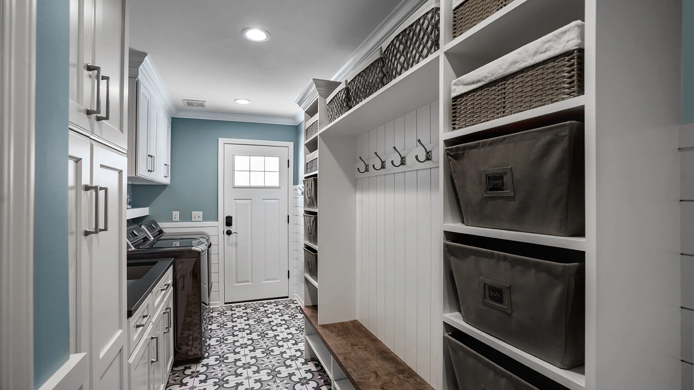 Inverness Mudroom Laundry Room: White cabinets, patterned tile floor, custom storage, baskets, hooks, and wood bench.