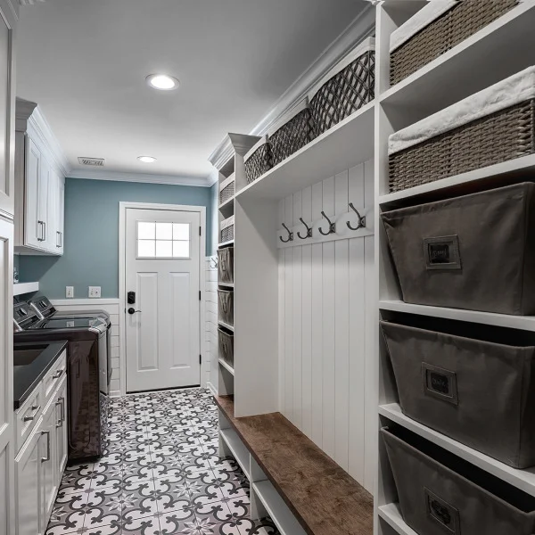 Inverness Mudroom Laundry Room: White cabinets, patterned tile floor, custom storage, baskets, hooks, and wood bench.