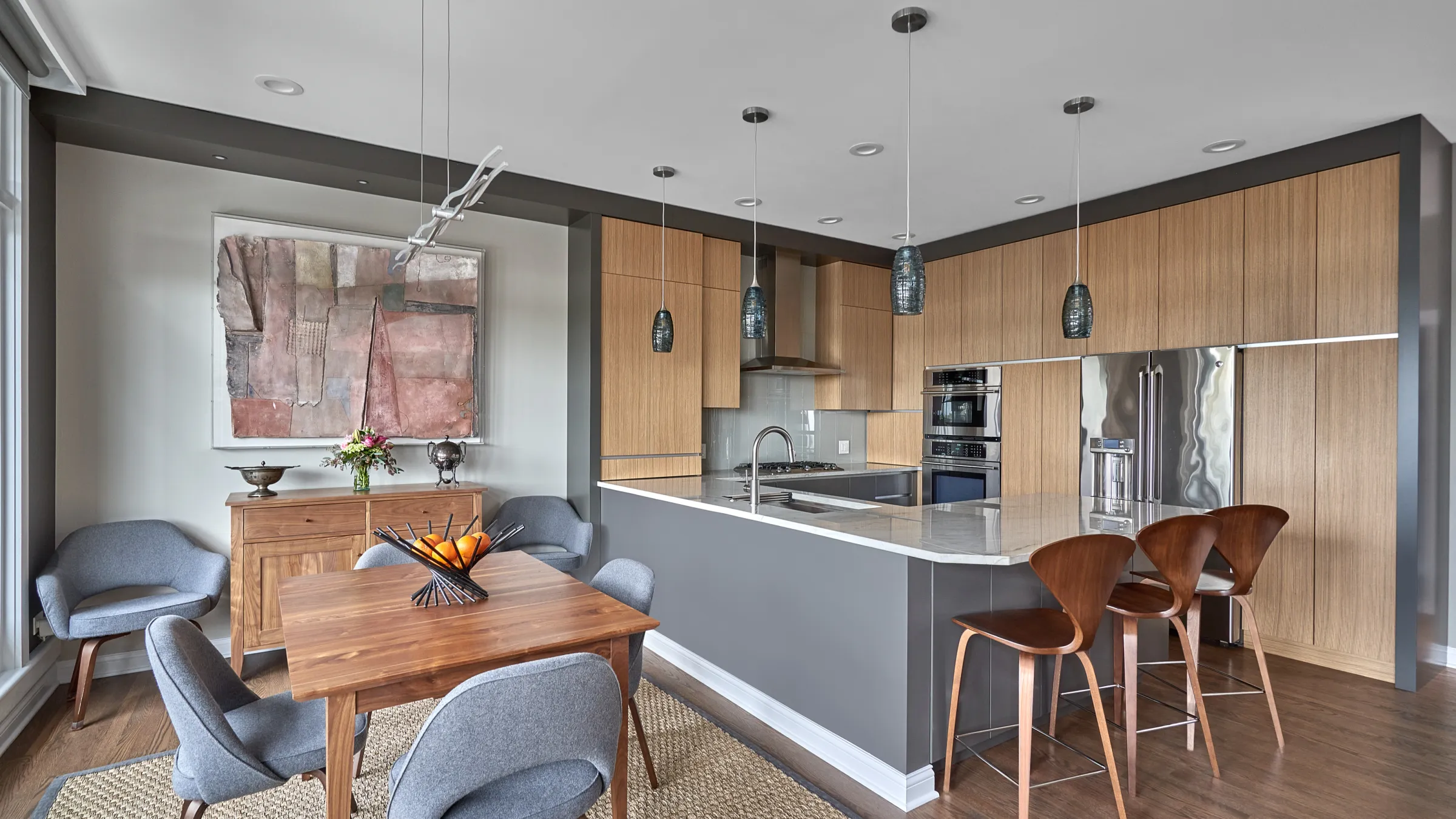 Modern condo kitchen and dining area with wood cabinets, gray island, marble countertop, wood floors, and gray upholstered ch