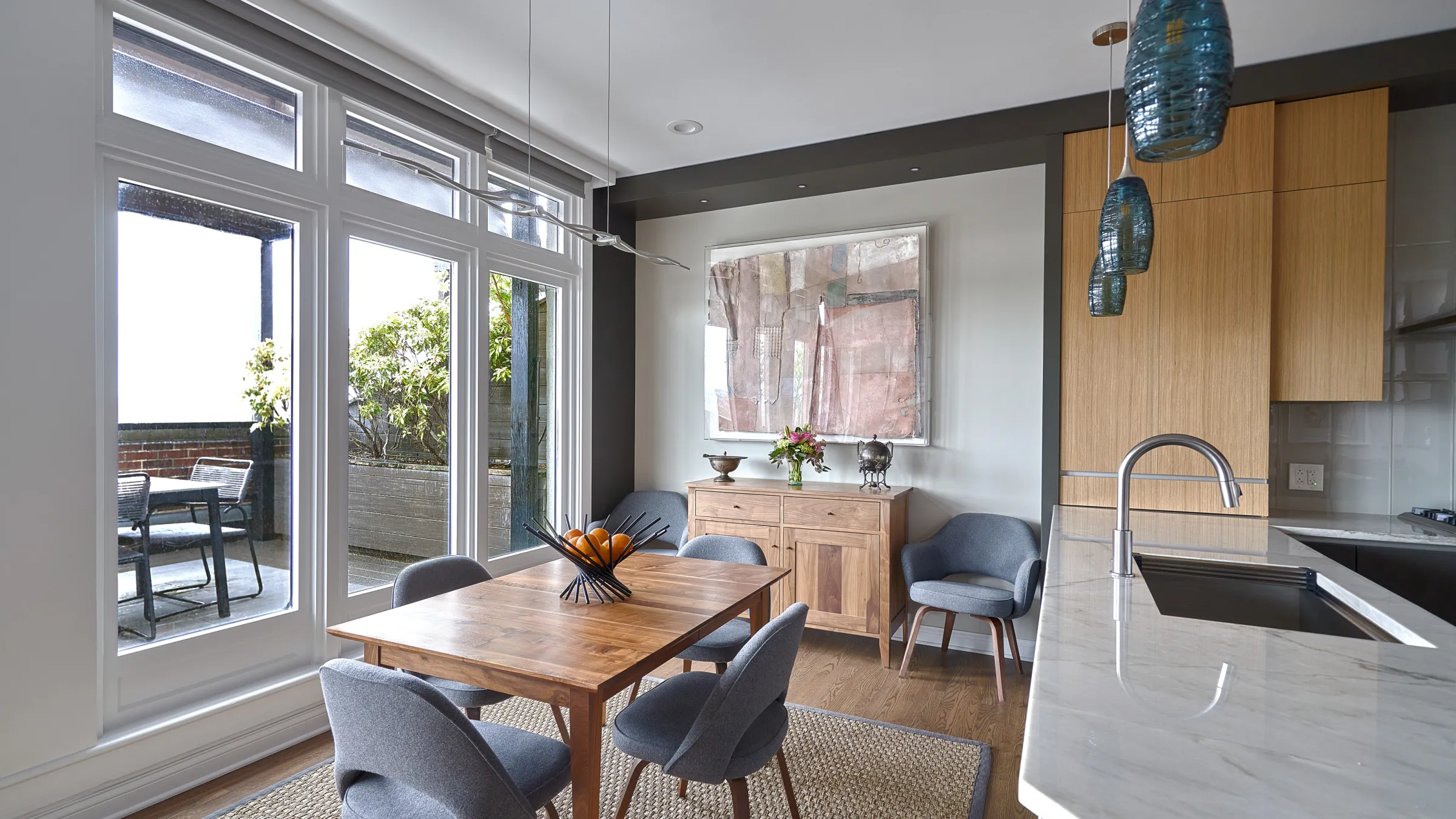 Bright Chicago condo dining area with wood table, gray chairs, light wood cabinets, and marble countertop.