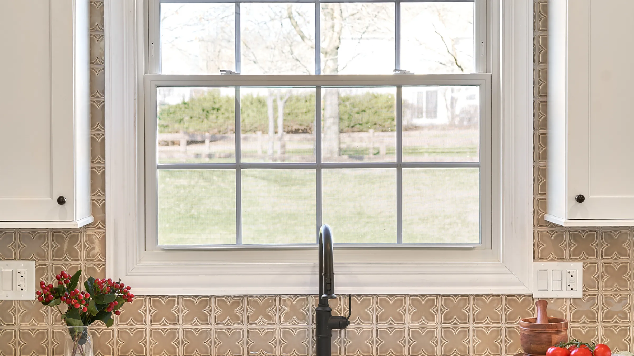 Kitchen remodel featuring a double-hung window, bronze backsplash, and white cabinets in Barrington, IL.