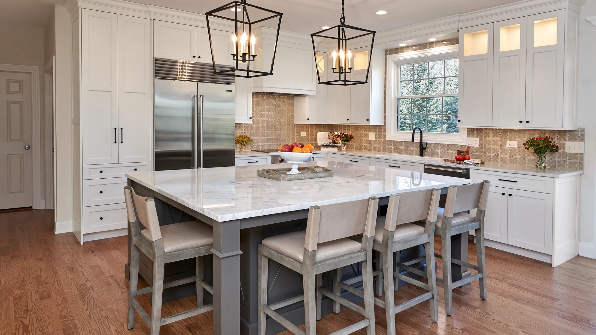Bright kitchen remodel in Barrington, IL featuring white cabinets, marble island, wood floors, and black pendant lights.