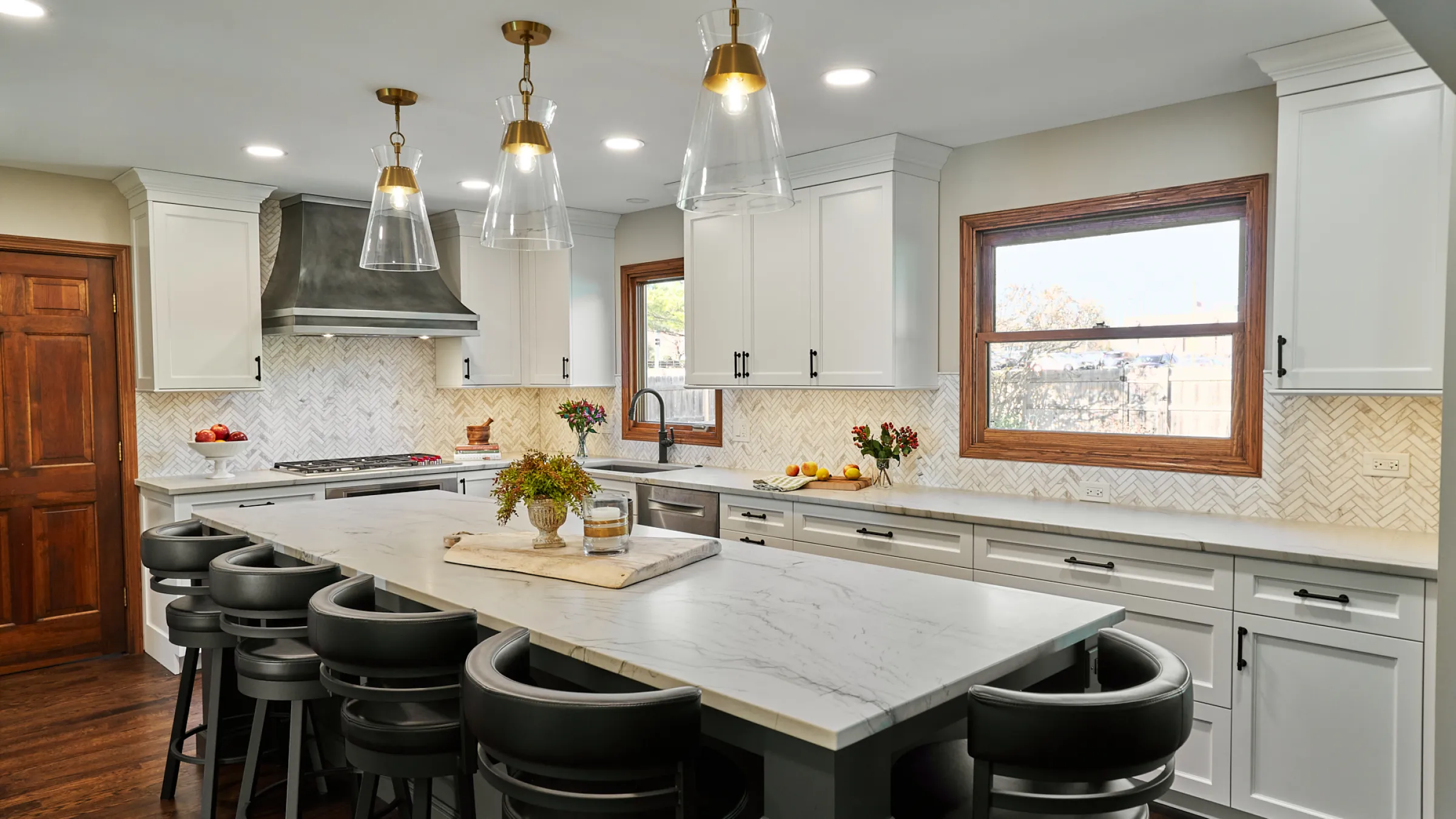 Bright kitchen remodel featuring white cabinets, marble countertops, herringbone backsplash, and black swivel stools.