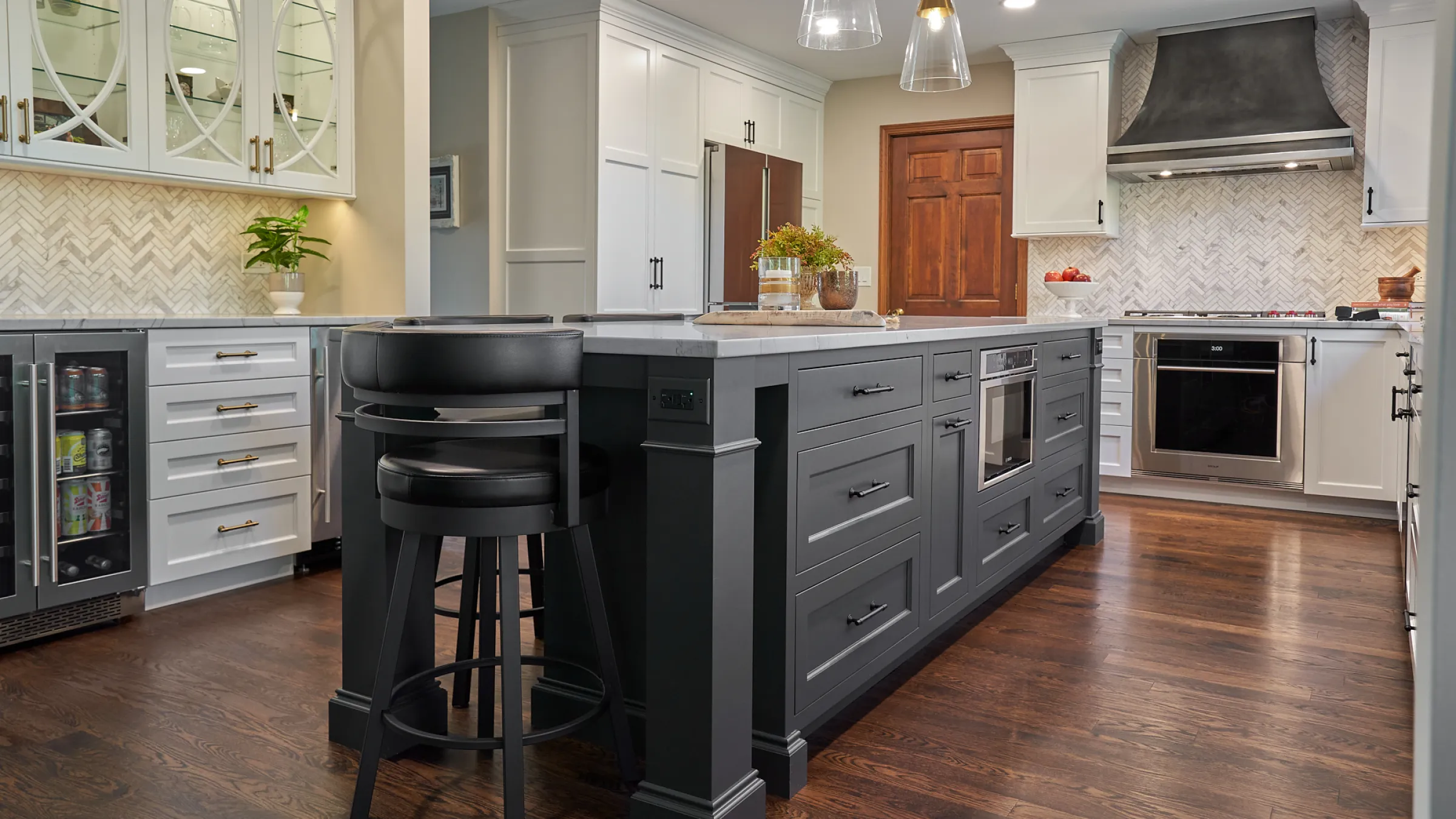 Modern kitchen remodel with gray island, white cabinets, herringbone backsplash, and stainless steel appliances.