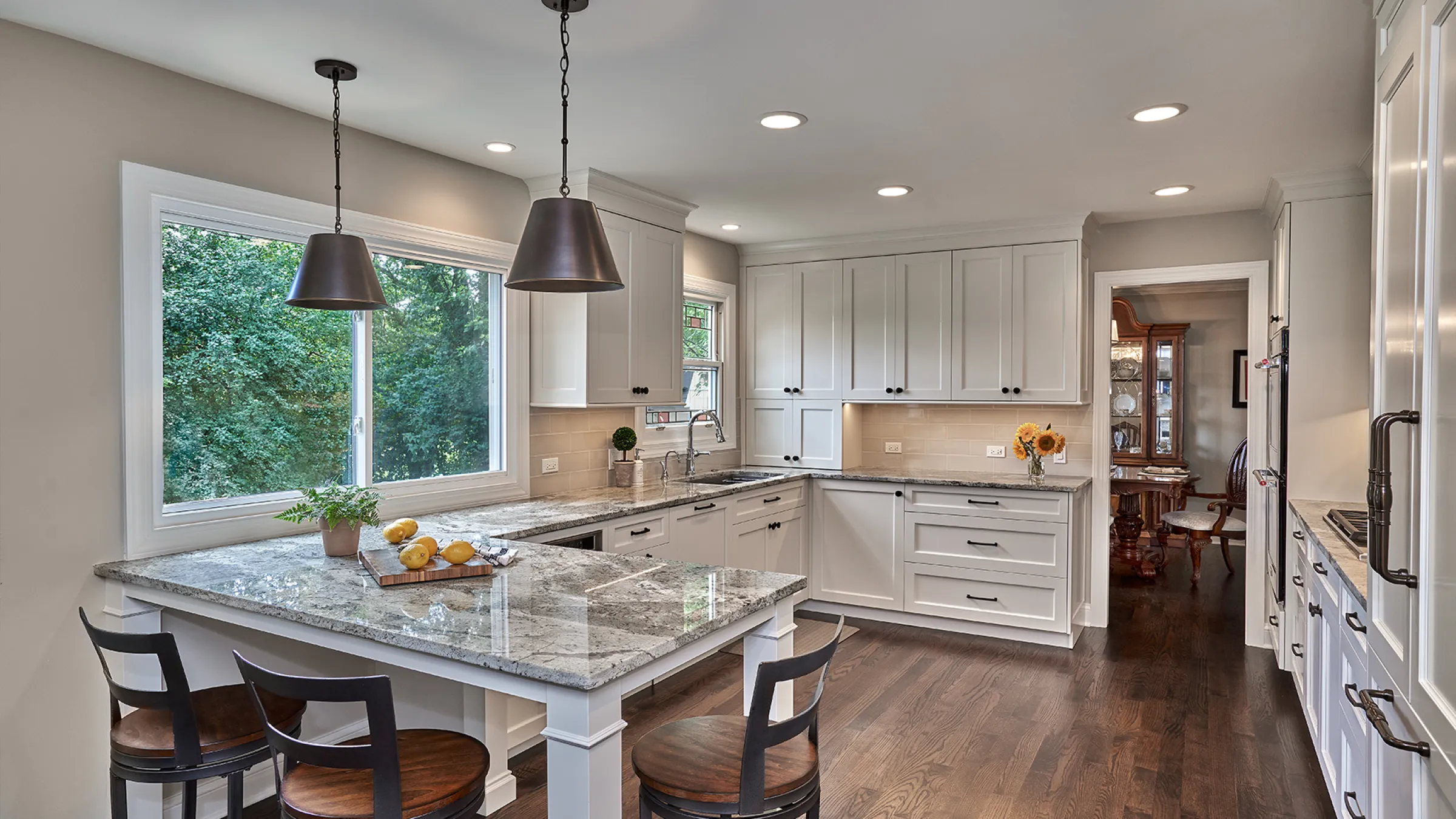 Bright, renovated kitchen with white cabinets, granite countertops, dark wood floors, and a large window.