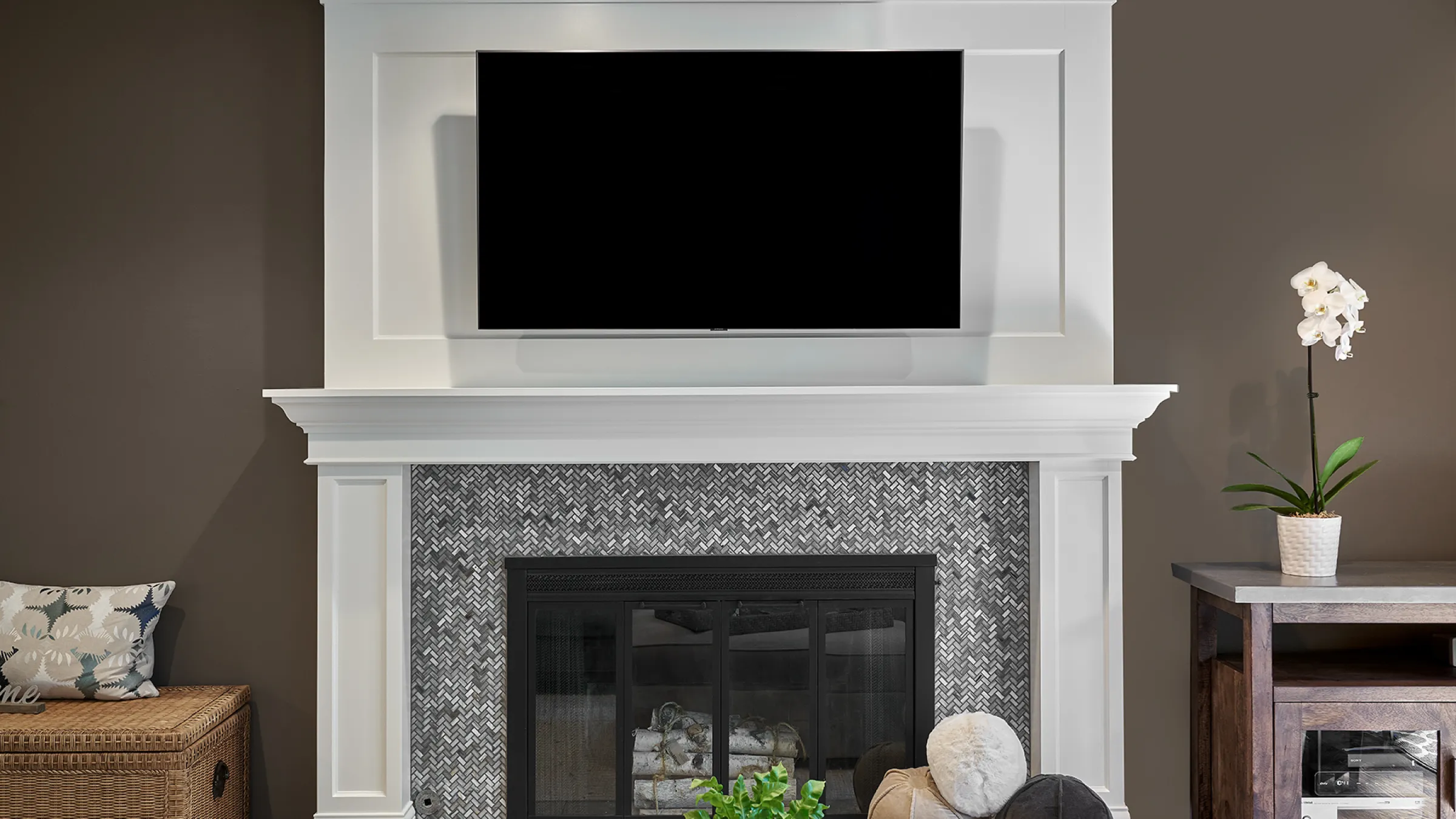Living room fireplace with white mantel, grey herringbone tile, and mounted TV. Modern interior design.