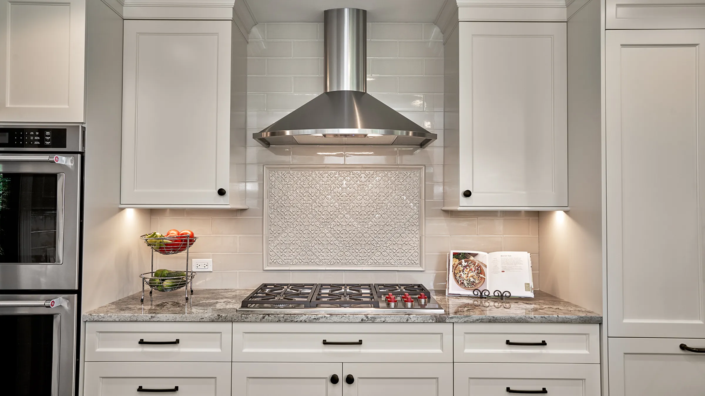 Modern kitchen remodel with white cabinets, stainless steel range hood, granite counters, & decorative tile backsplash.