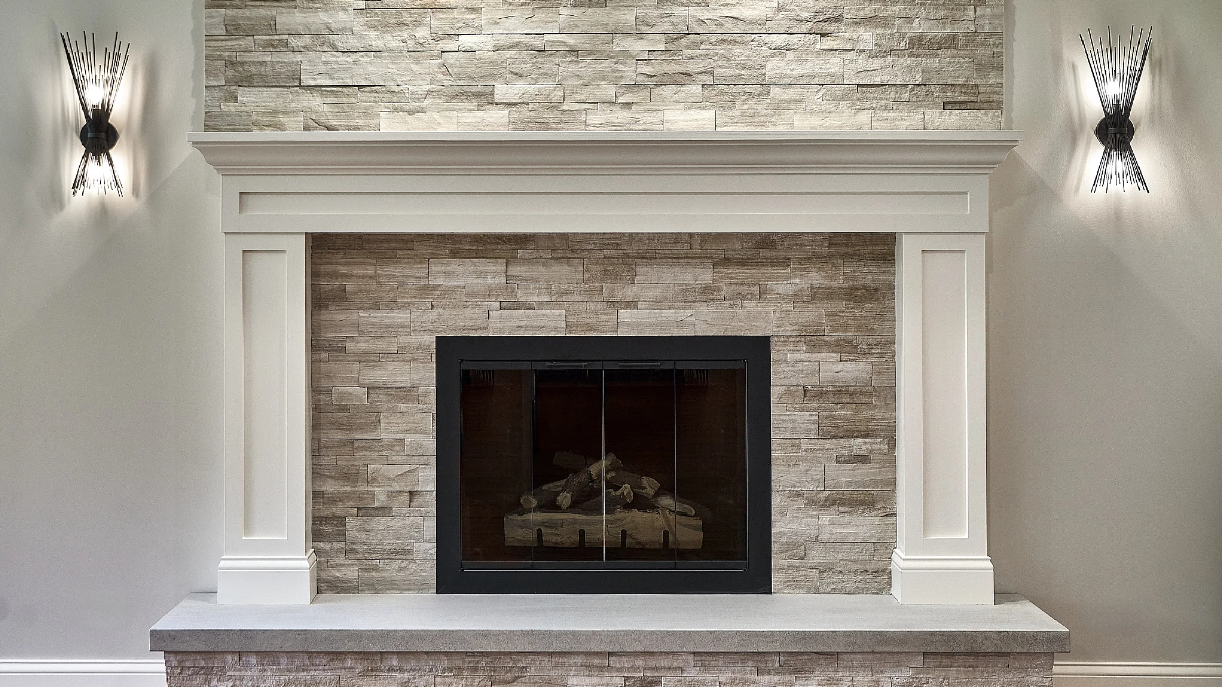 Inverness fireplace remodel: Stone surround, modern sconces, white mantle. GS Construction, Chicago-area home renovation.