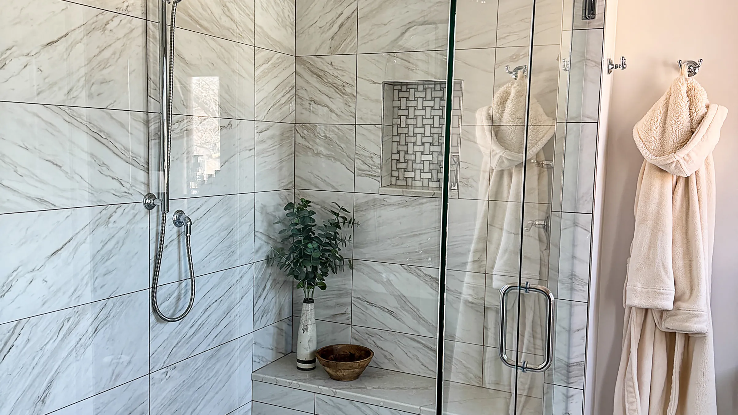 Modern bathroom remodel featuring marble tile shower with glass door and cozy robes.