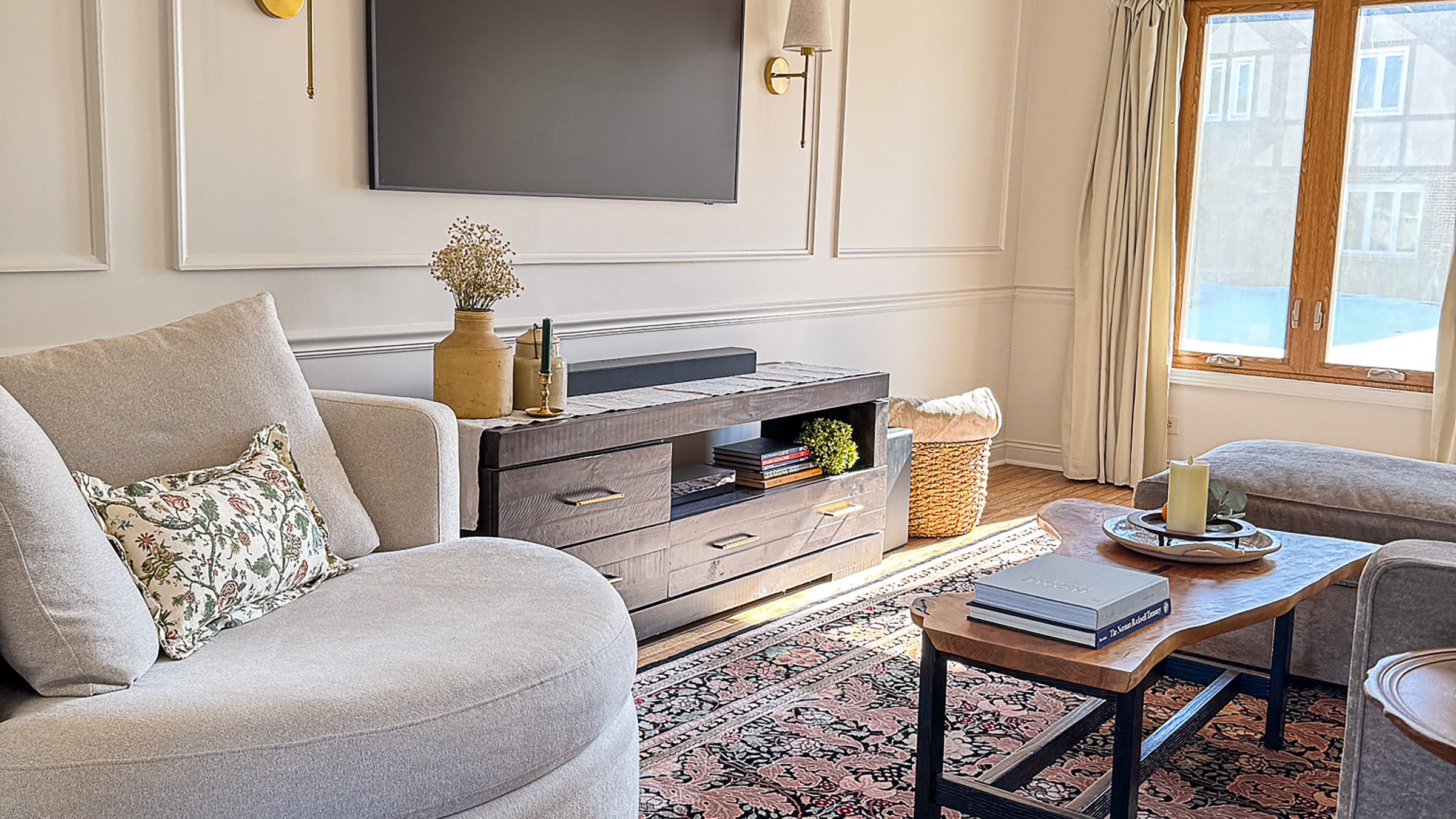 Cozy living room with custom console table, patterned rug, and a beige swivel chair with a floral throw pillow.