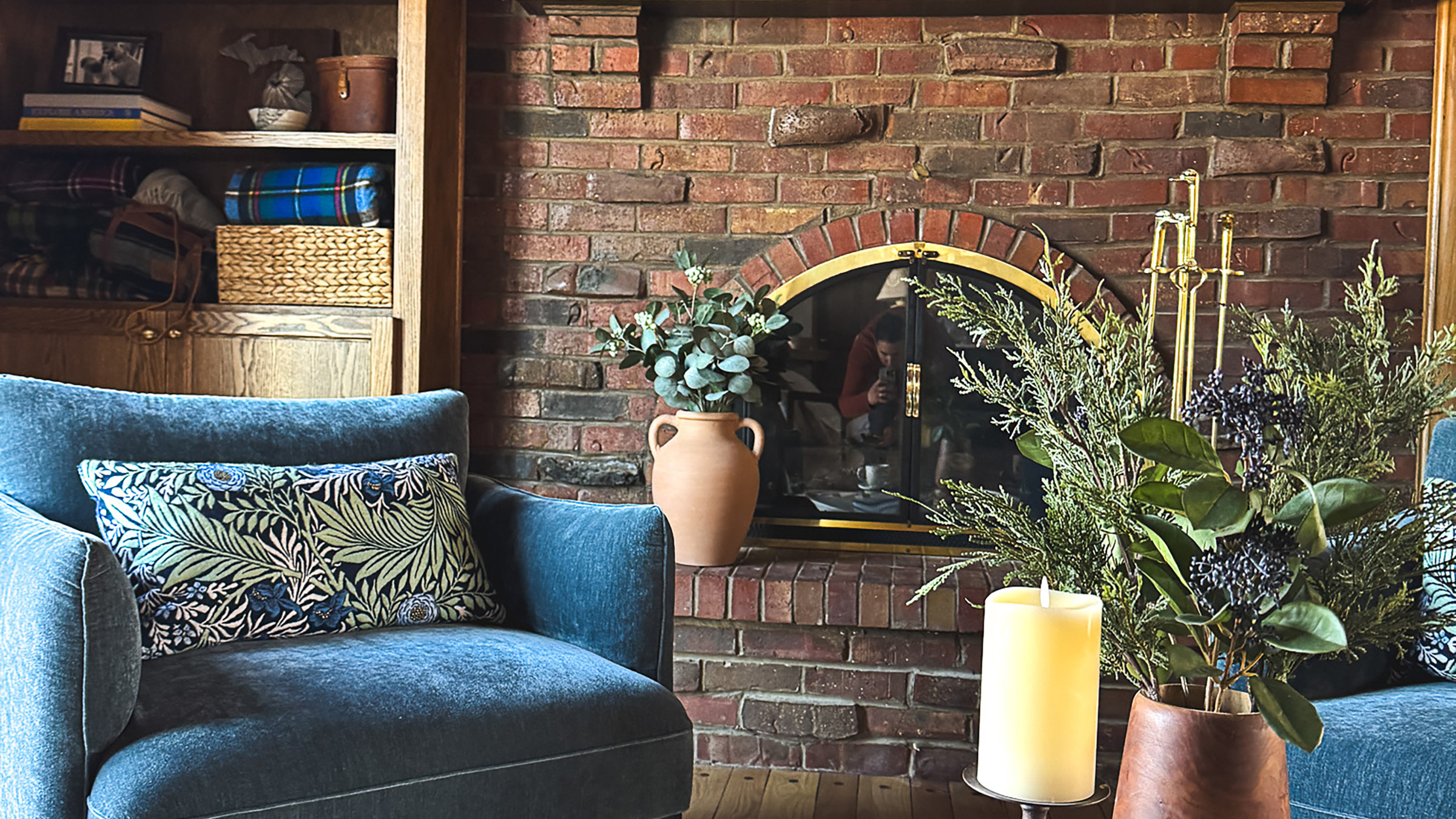 Cozy living room with brick fireplace, blue armchair with floral pillow, and rustic decor. Warm, inviting interior design.