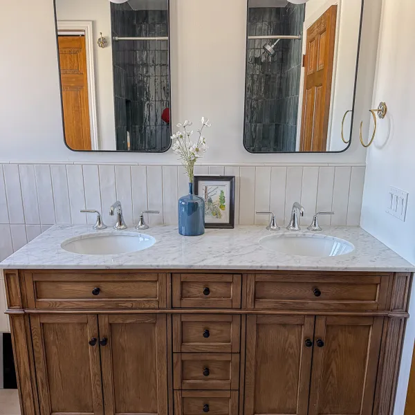 Bathroom remodel with double vanity, marble countertop, wood cabinets, and modern fixtures.