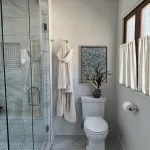 Bathroom remodel featuring a glass shower, robe, framed art, and toilet with decorative vase in Arlington Heights.