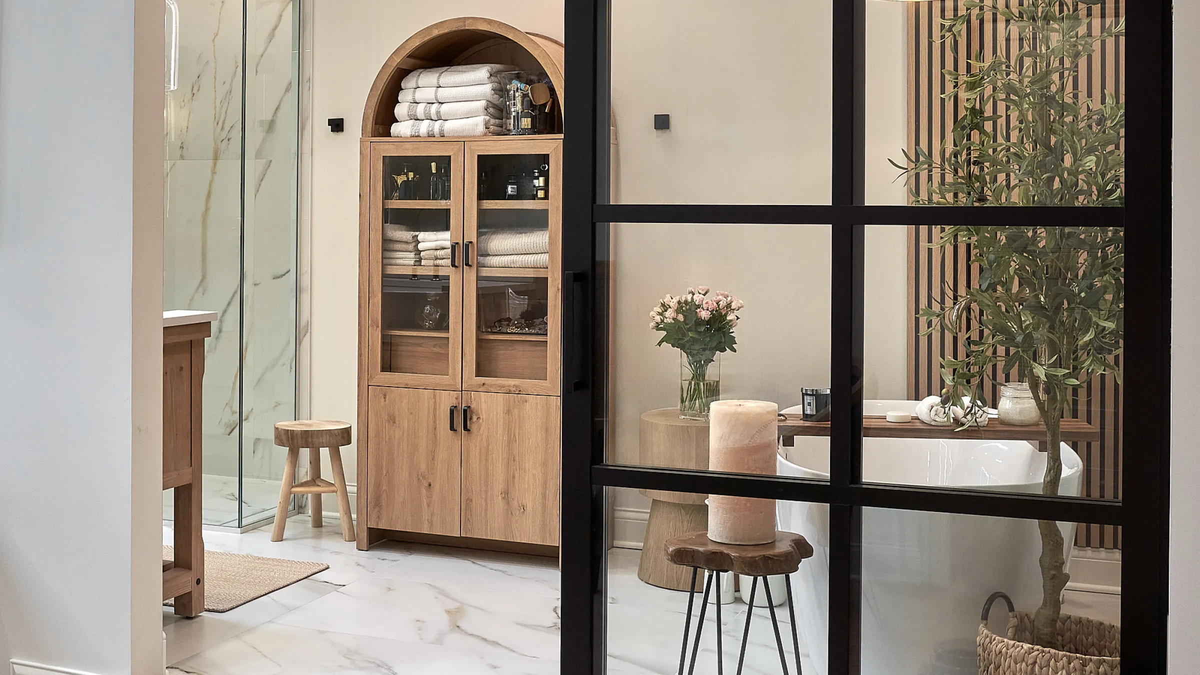 Bright bathroom remodel with wood cabinet, marble floors, glass shower, and black framed glass door.