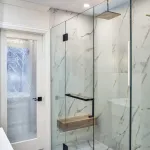Modern bathroom remodel featuring a glass shower door, patterned glass door, and light marble tile.