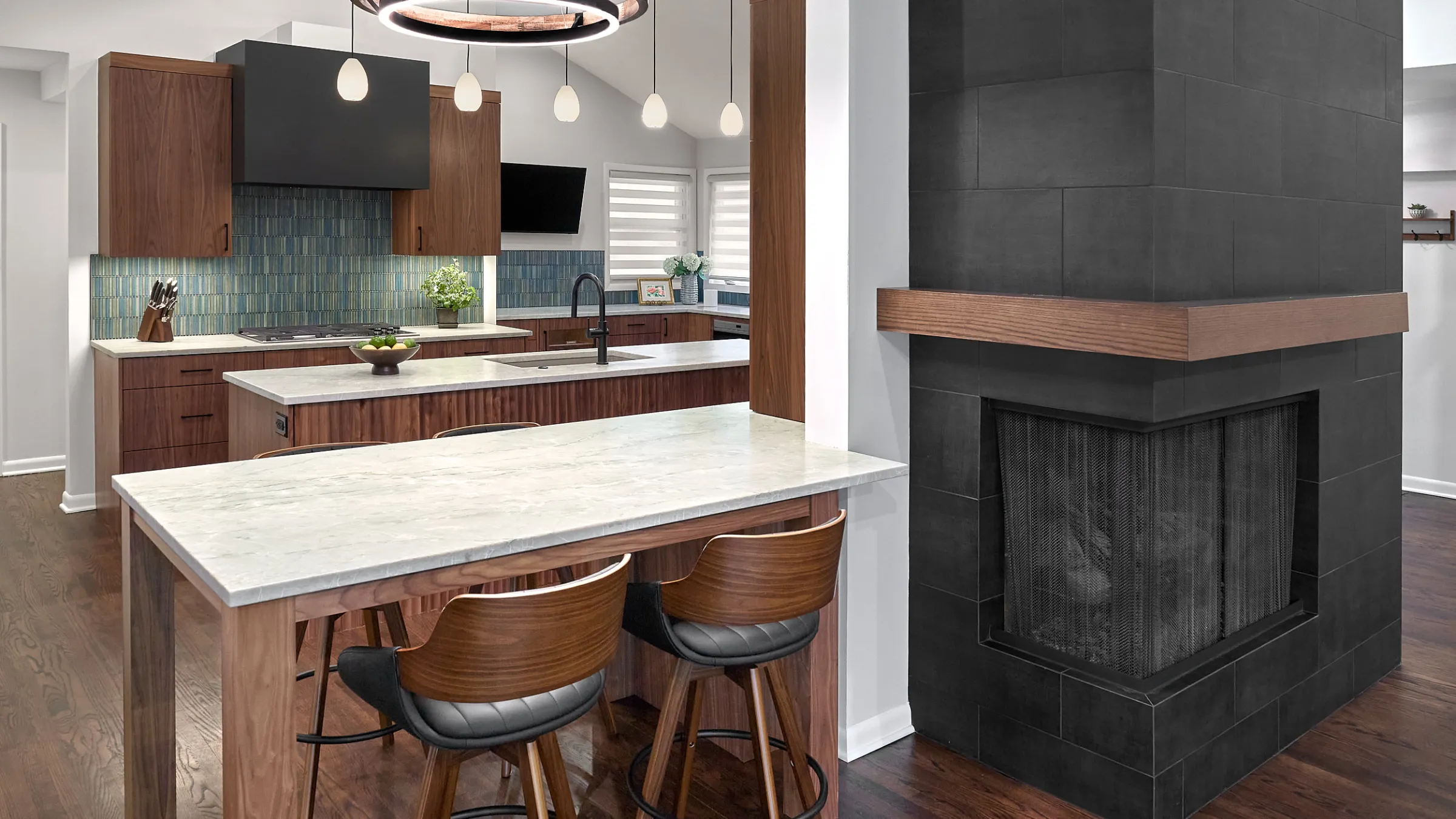 Modern kitchen remodel with walnut cabinets, marble countertops, blue tile backsplash, and a black tiled fireplace.
