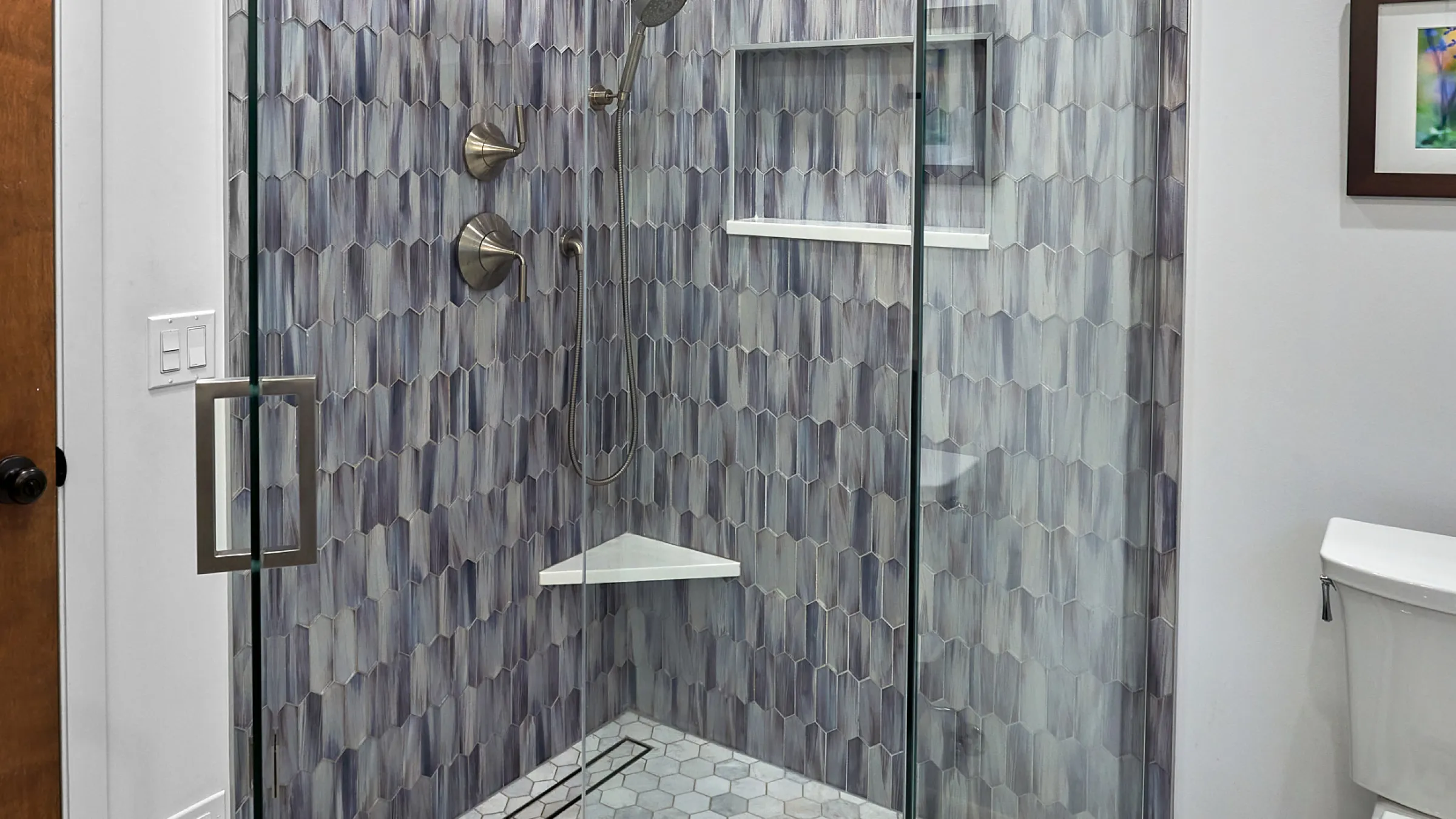 Modern shower remodel with elongated hexagon tile, glass door, and built-in shelving. Updated bathroom in Mount Prospect.