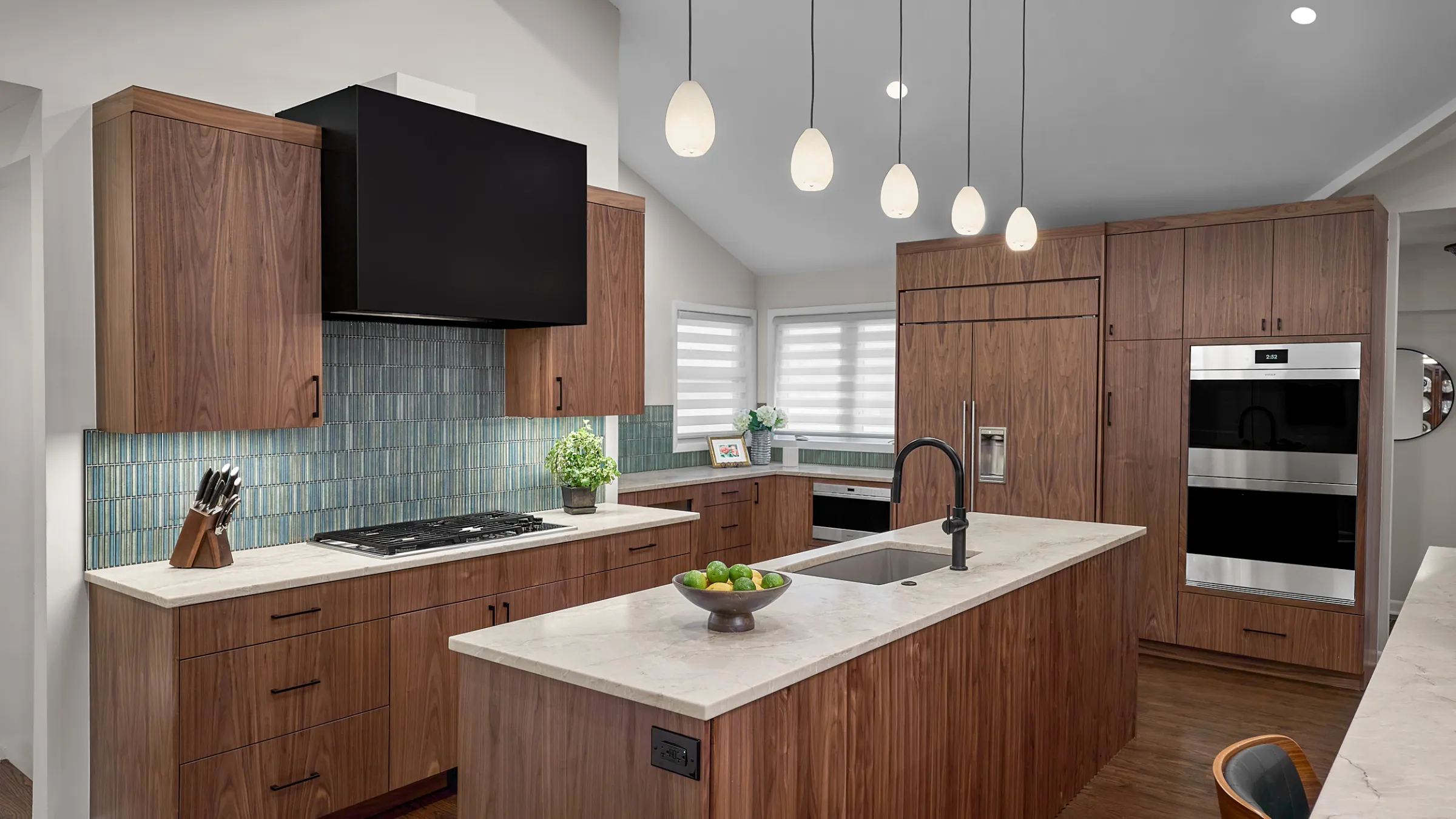 Modern kitchen remodel with walnut cabinets, waterfall countertops, black range hood, and island with sink.