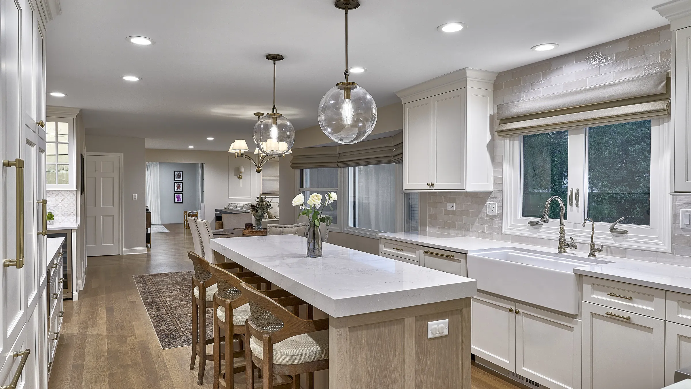 Modern white kitchen with large island, brass globe pendants, white shaker cabinets, farmhouse sink, and wood floors.