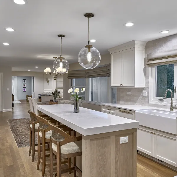 Modern white kitchen with large island, brass globe pendants, white shaker cabinets, farmhouse sink, and wood floors.