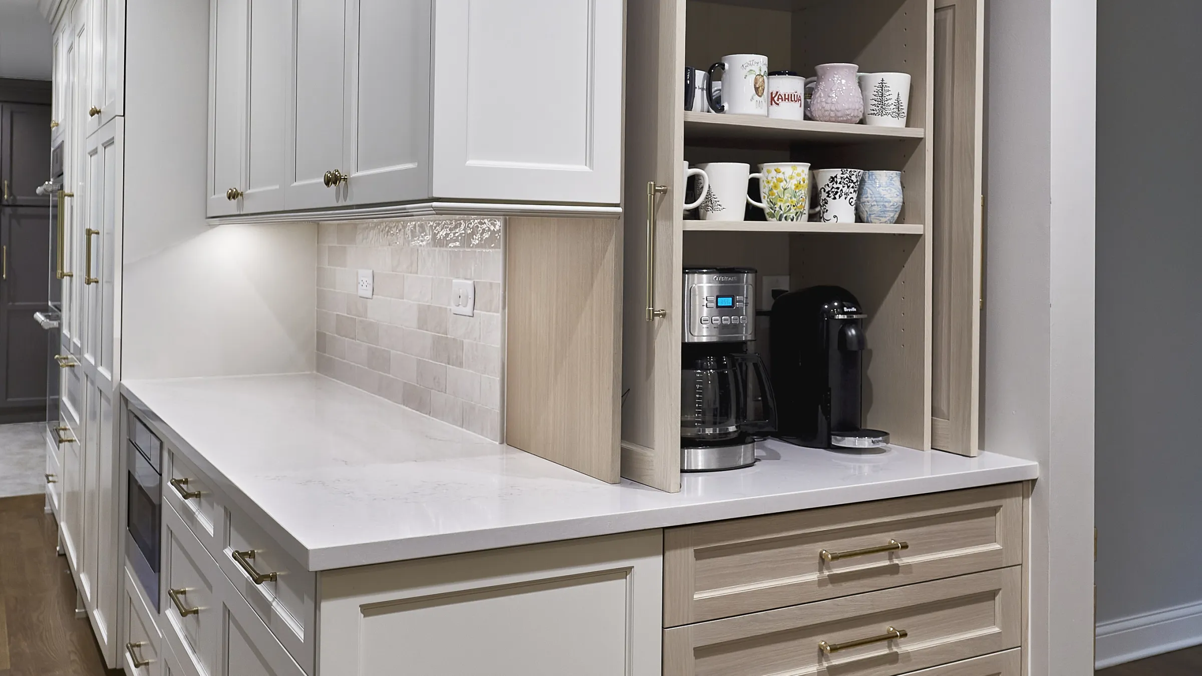 Modern kitchen with white shaker cabinets, light wood grain pull-out coffee bar, white quartz countertops, and subway tile ba