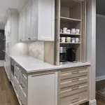 Modern kitchen with white shaker cabinets, light wood grain pull-out coffee bar, white quartz countertops, and subway tile ba