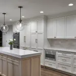 Modern white kitchen with large island, brass globe pendants, built-in appliances, light wood cabinets & white quartz counter