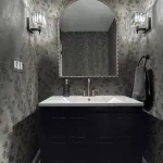 Modern powder room with dark floral wallpaper, white vanity top, dark blue cabinet, brushed nickel faucet, and towel ring.