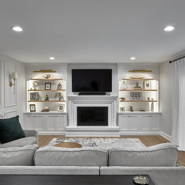 Modern living room with white built-in entertainment center, fireplace, recessed lighting, light gray sofa, and sheer white c