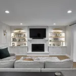 Modern living room with white built-in entertainment center, fireplace, recessed lighting, light gray sofa, and sheer white c