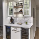 Wet bar with white shaker cabinets, quartz countertop, patterned tile backsplash, beverage fridges, and liquor bottles.