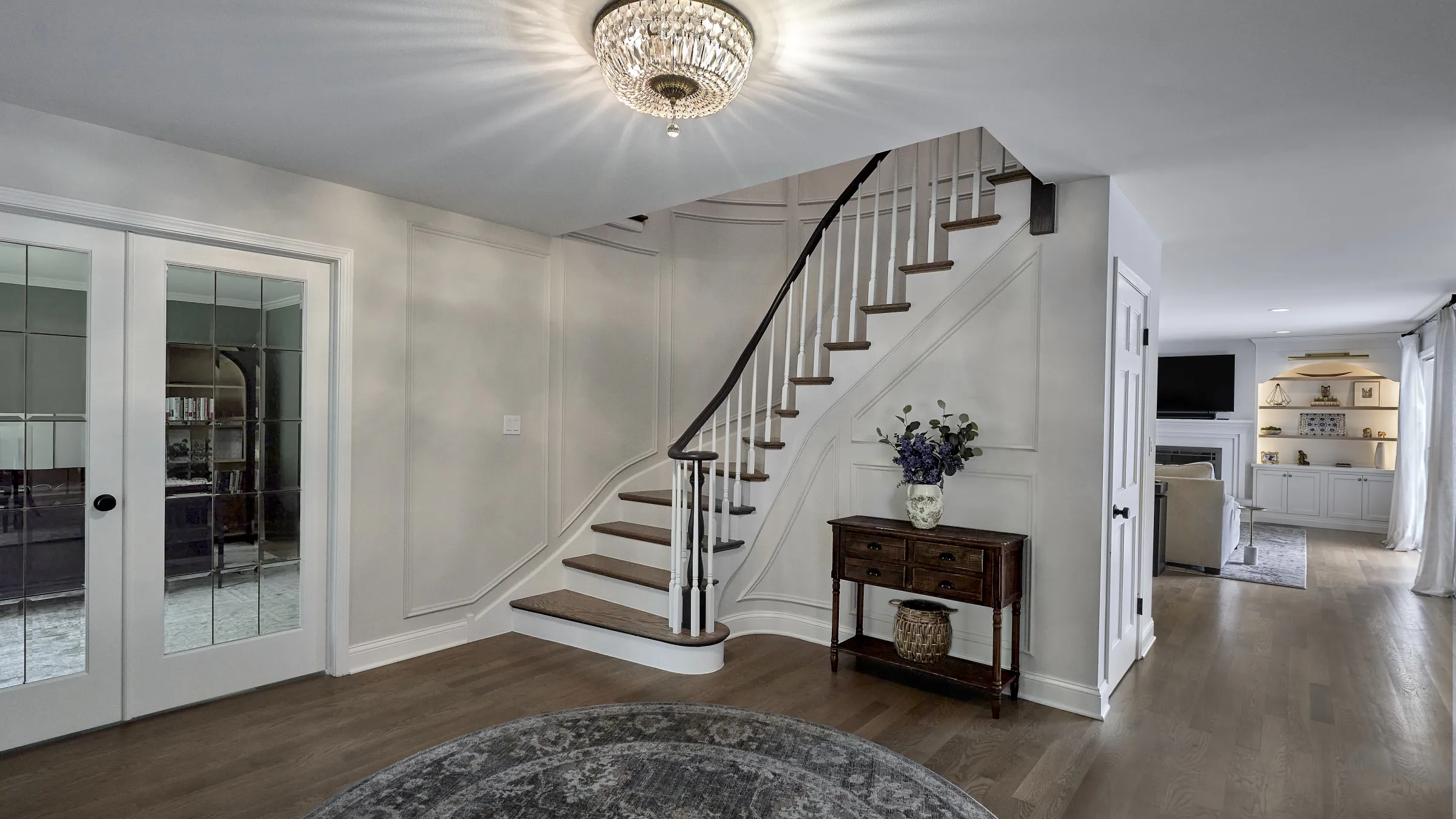 Elegant foyer with dark hardwood floors, a curved staircase with white risers and dark treads, and a crystal chandelier.