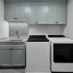 Modern laundry room with light gray shaker cabinets, white quartz countertop, patterned backsplash, stainless steel sink, and