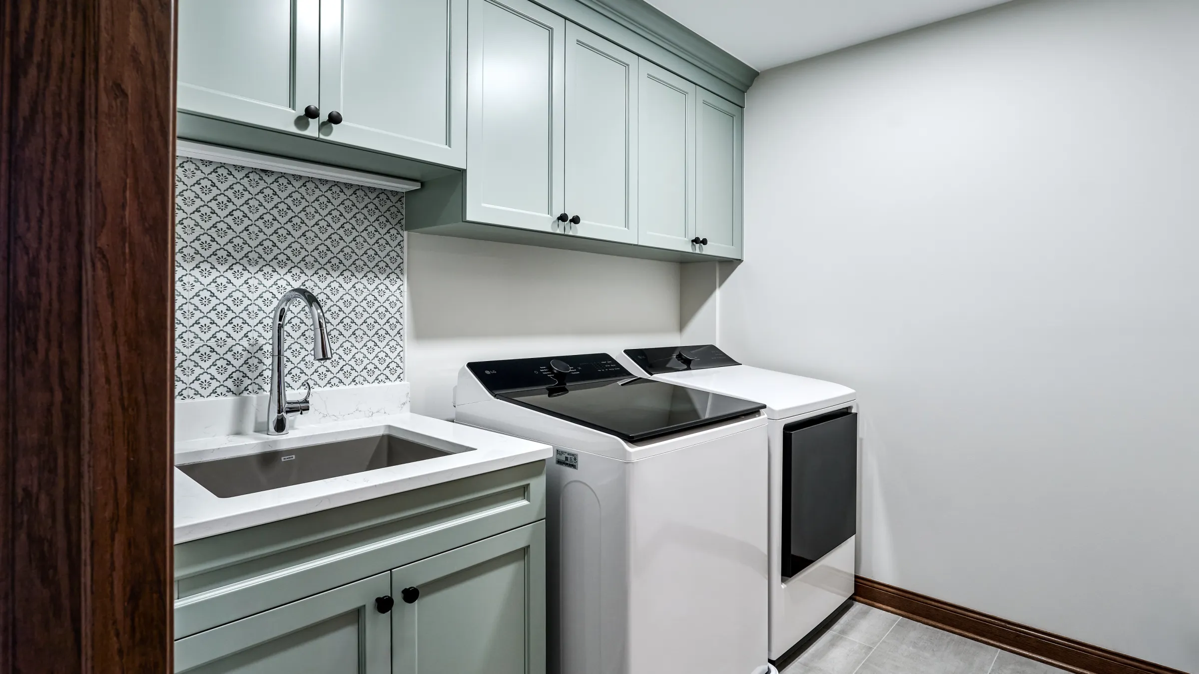 Modern laundry room with mint green shaker cabinets, white quartz countertop, stainless sink, patterned backsplash, and LG wa