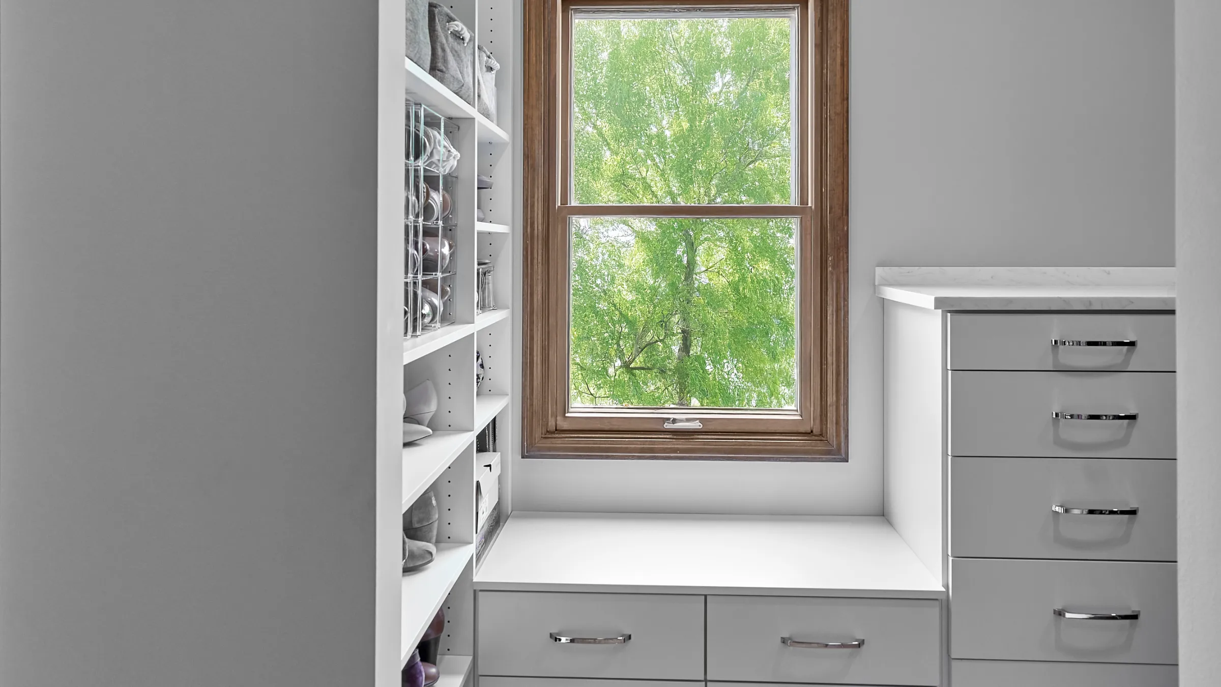 Custom closet with white shelving, clear shoe organizers, gray storage bins, and light gray drawers with chrome pulls.