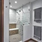 Modern primary bathroom shower with white marble-look tiles, a built-in bench with hexagonal wood-look tiles, and chrome fixt